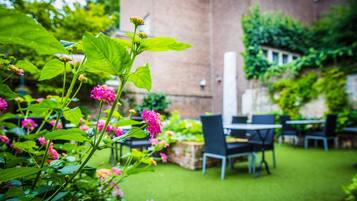Un jardín con muro de ladrillo, mobiliario exterior y plantas en flor.