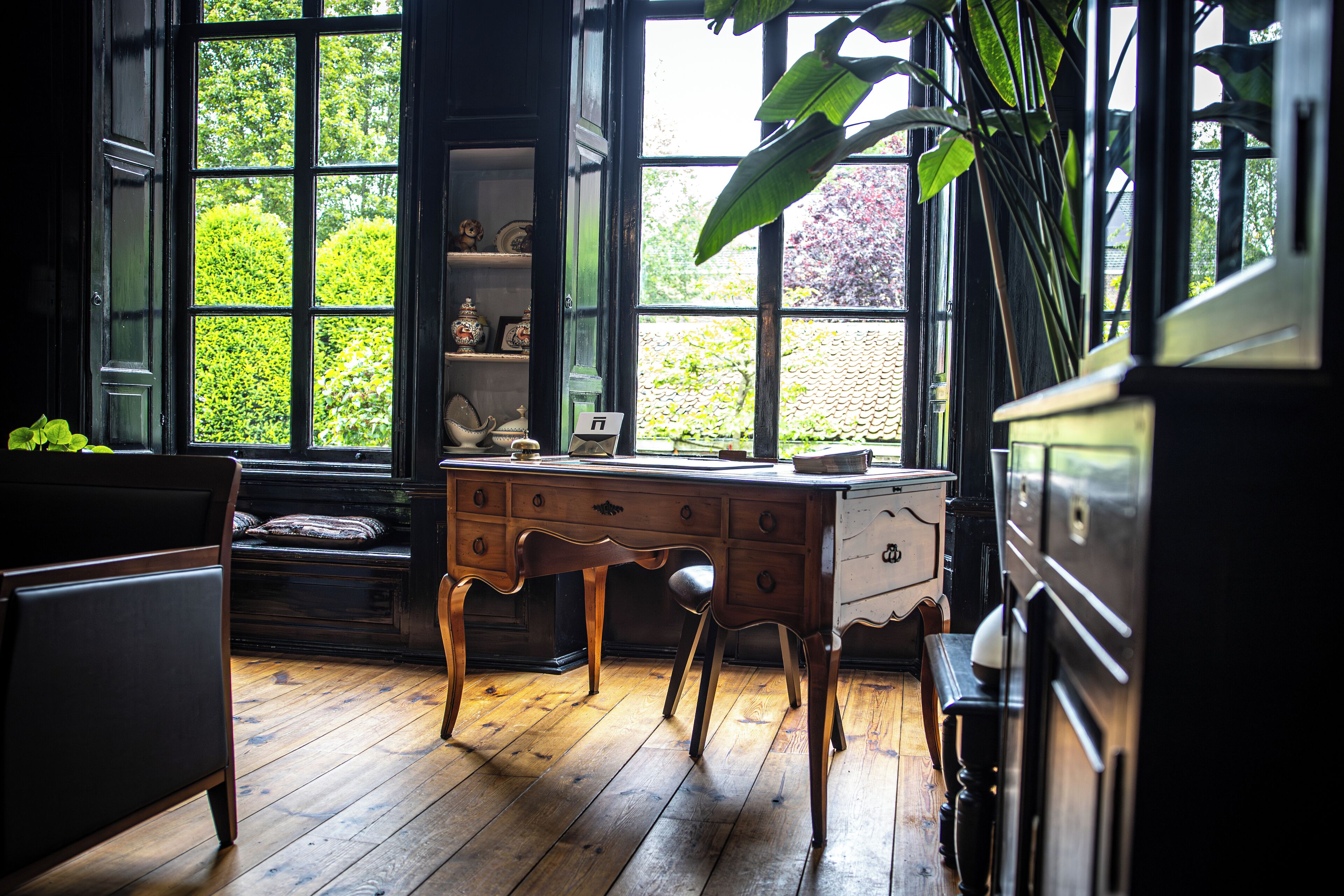 Une pièce avec un bureau en bois, une chaise et une commode. Il y a une fenêtre donnant sur un paysage verdoyant.