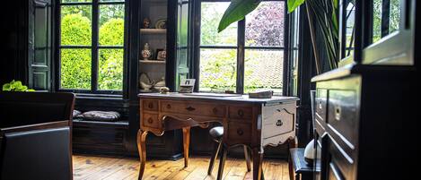 Une pièce avec un bureau en bois, une chaise et une commode. Il y a une fenêtre donnant sur un paysage verdoyant.
