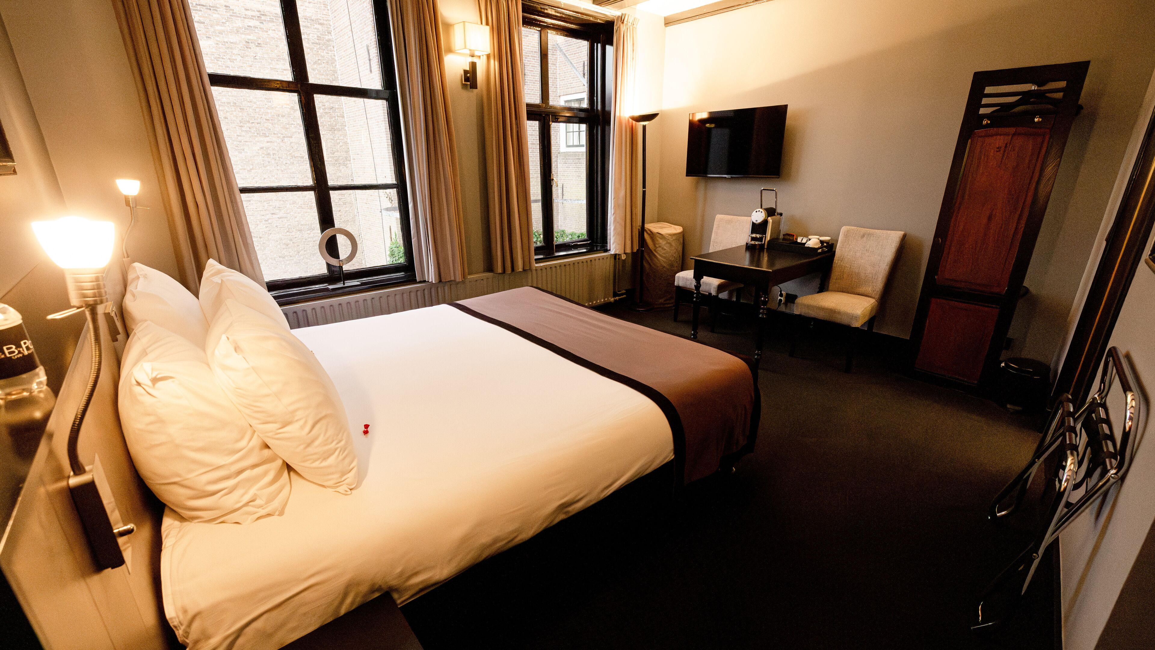 A hotel room with a large bed, a desk with a chair, a TV, and a window with curtains.