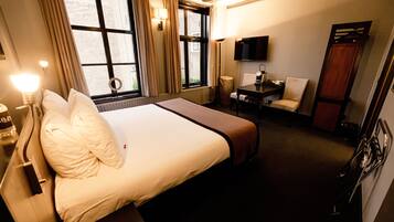 A hotel room with a large bed, a desk with a chair, a TV, and a window with curtains.