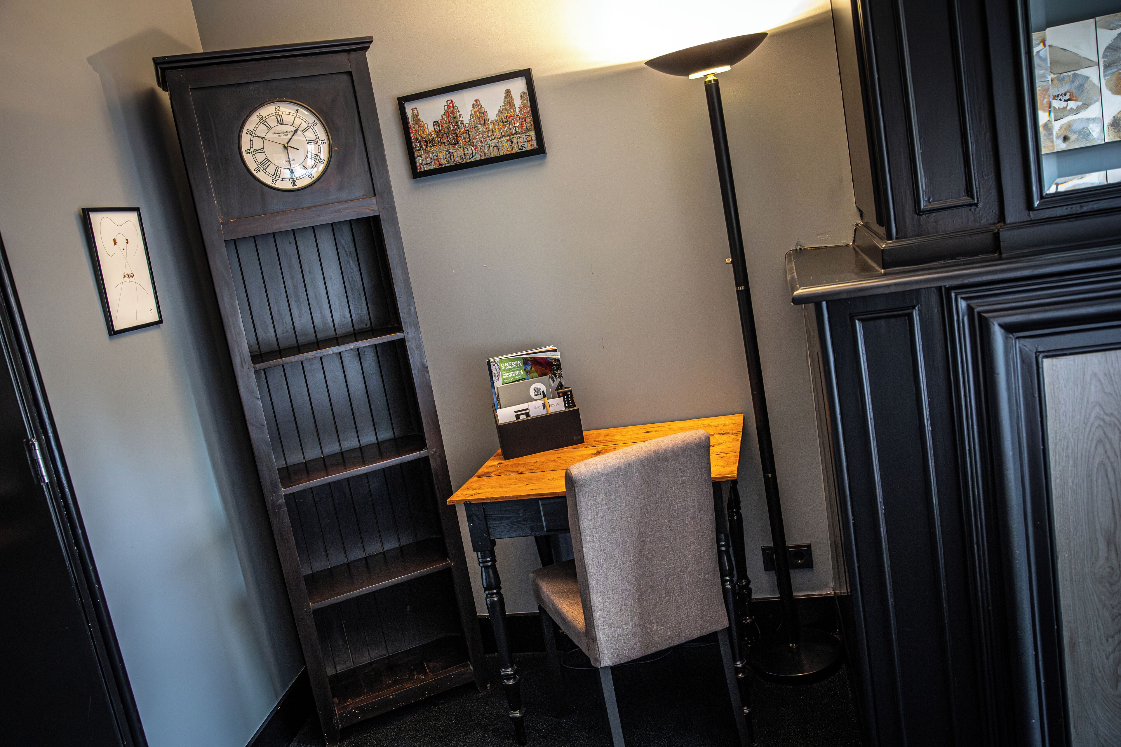 Een hoekzaal met een houten bureau, een stoel, een klok en een lijst met een afbeelding aan de muur.