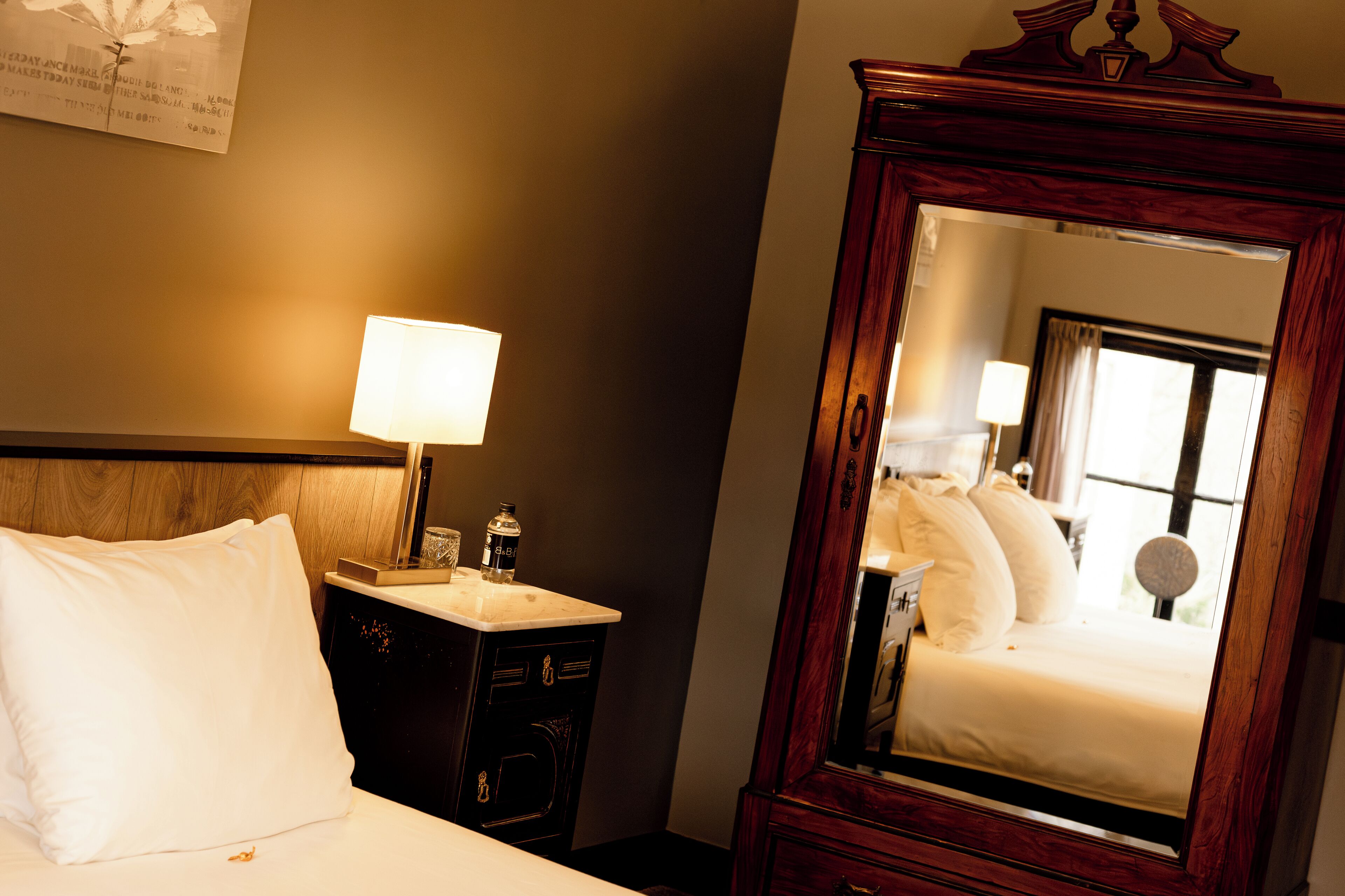 Een hotelkamer met een bed, een nachtkastje met een lamp, een dressoir en een grote spiegel.