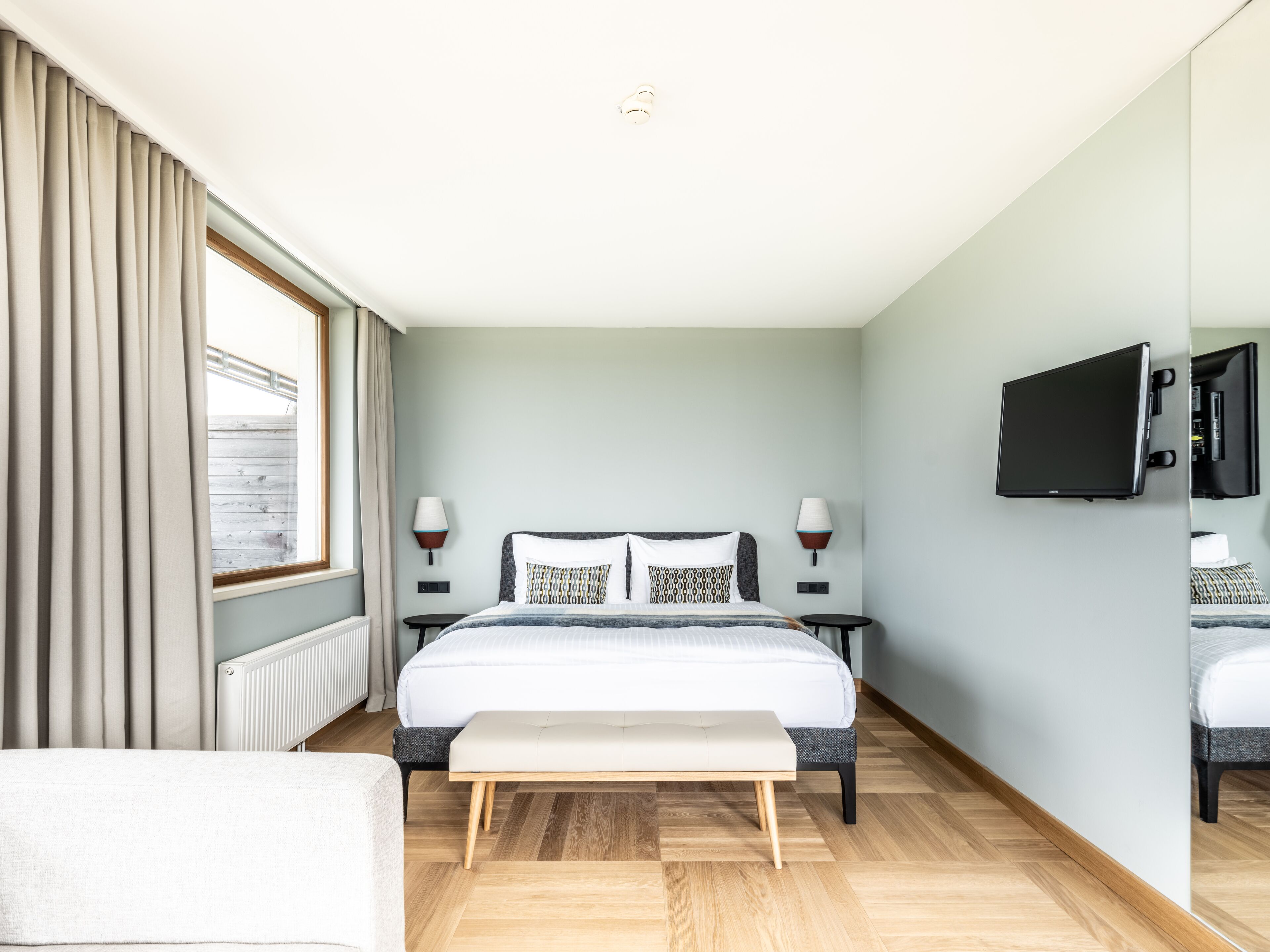 A modern hotel room with a large bed, bedside tables, a flat-screen TV, and a view of the outside.