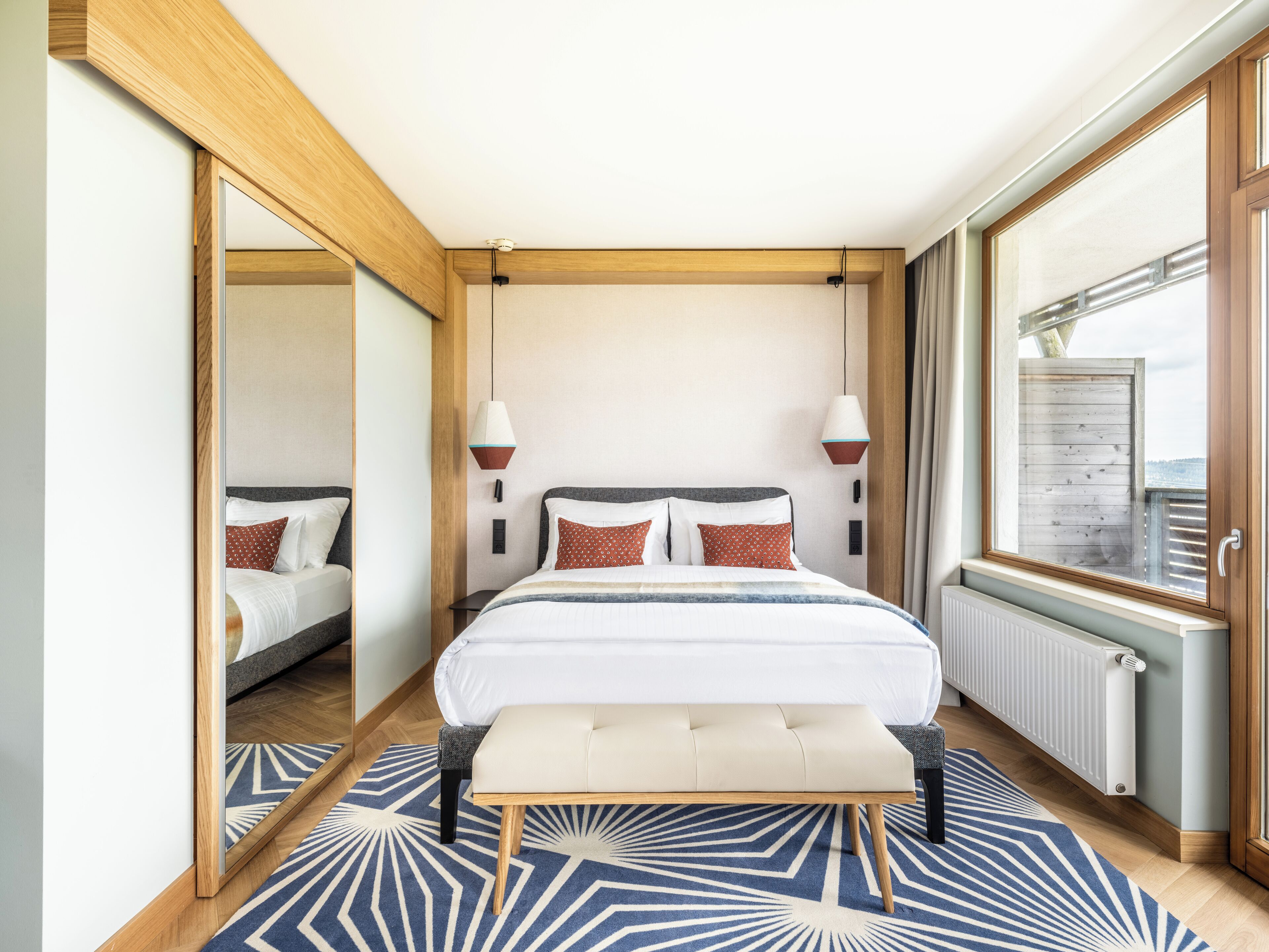 Habitación de hotel moderna con una cama grande, lámparas de noche, vistas por una ventana y un espejo en una pared.