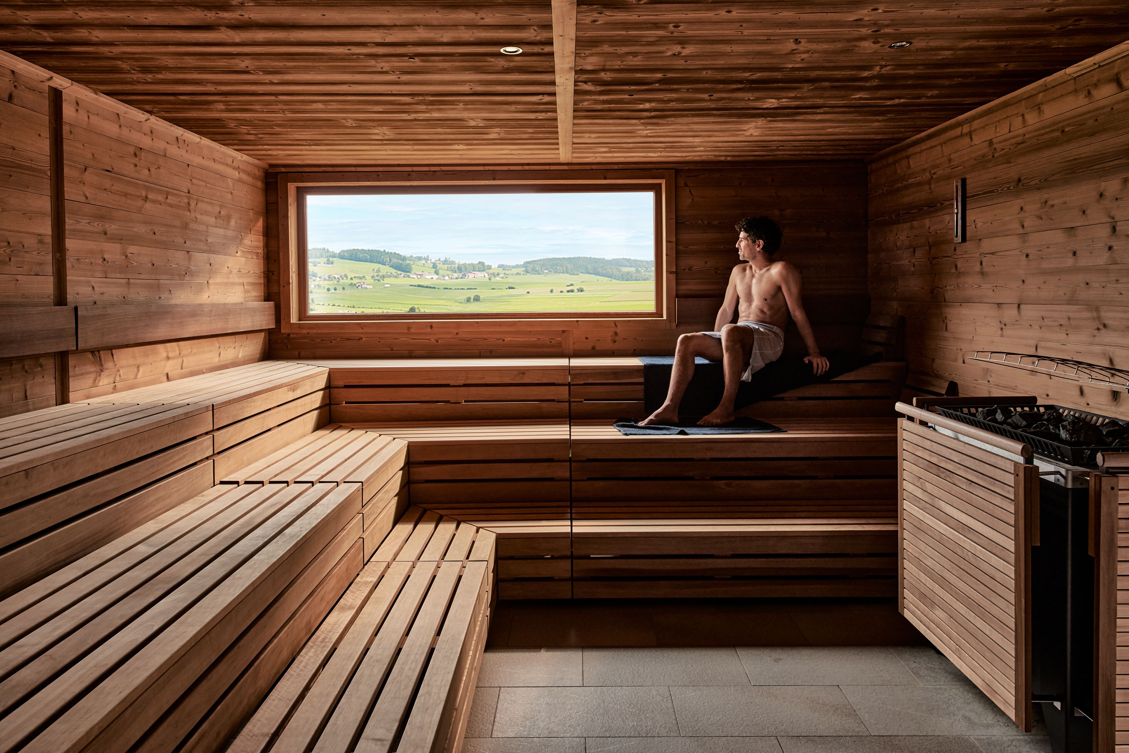 Un sauna avec des bancs en bois et une grande fenêtre donnant sur la campagne.