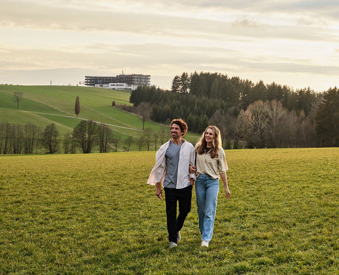 Um casal caminhando em um campo gramado com um edifício ao fundo.