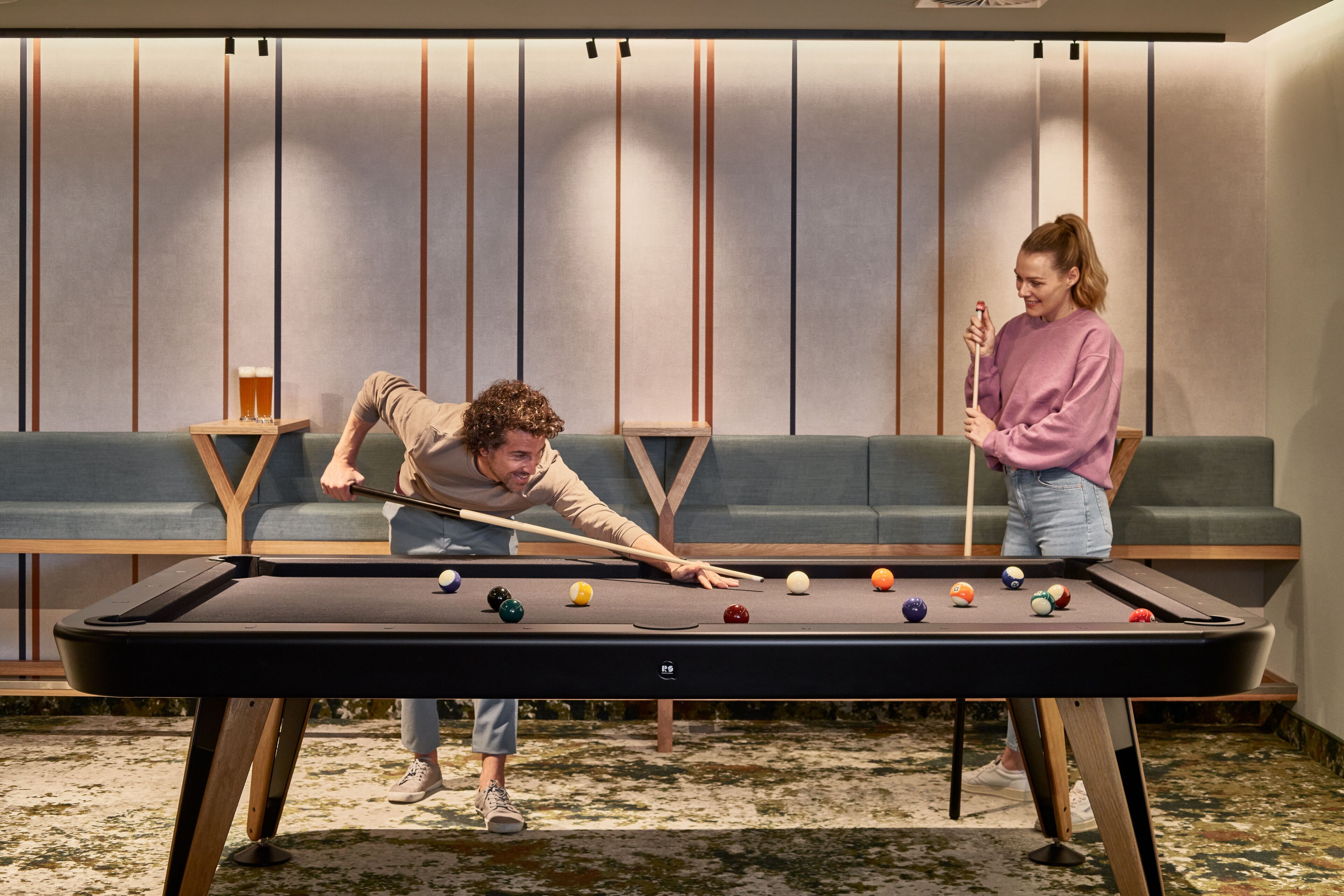 A pool table in a room with a sofa and a small table with a lamp.