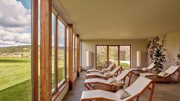 Una habitación soleada con ventanas amplias, sillones de madera y vistas a un paisaje verde.