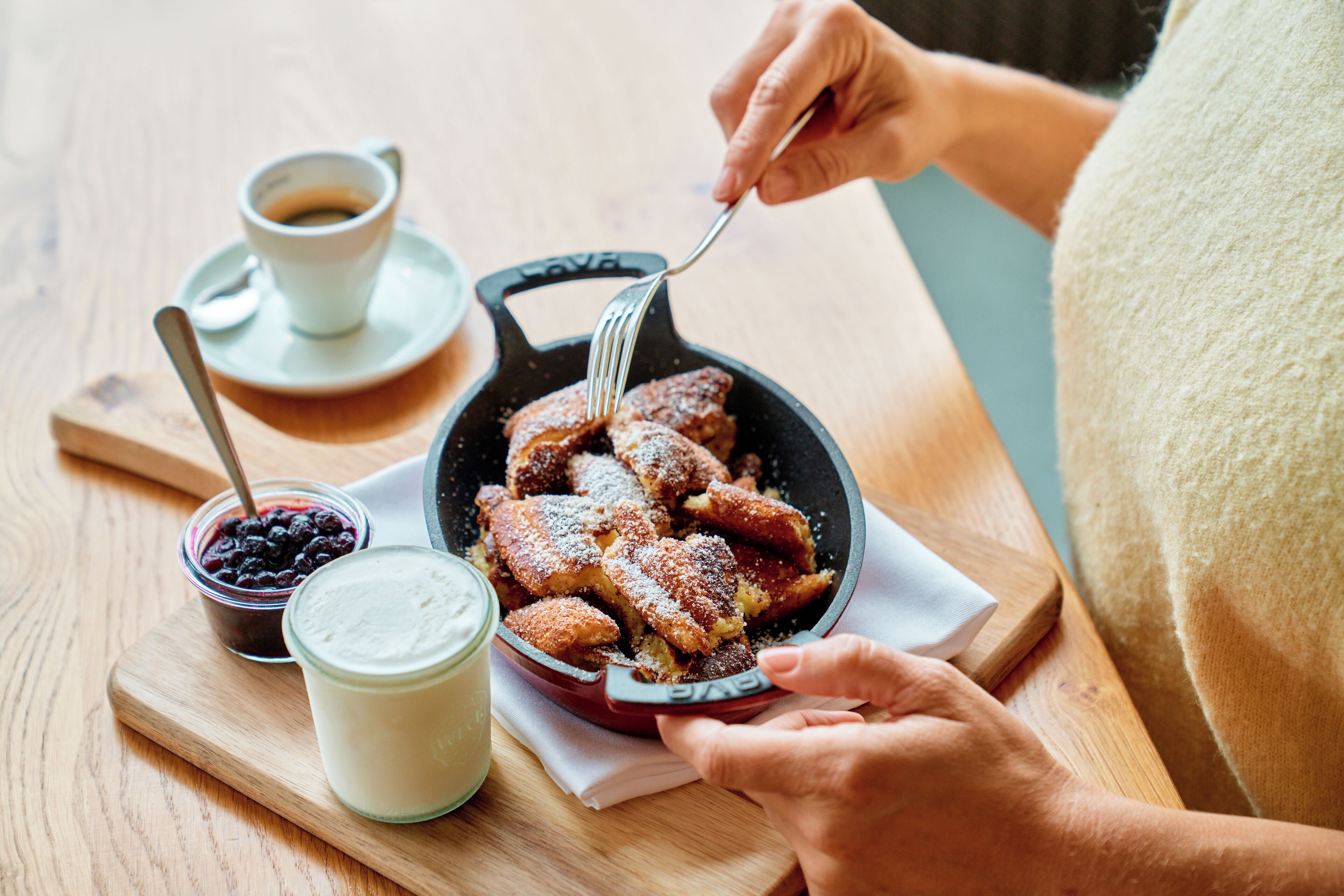 A person eating bread with jam and a cup of coffee on a wooden table.