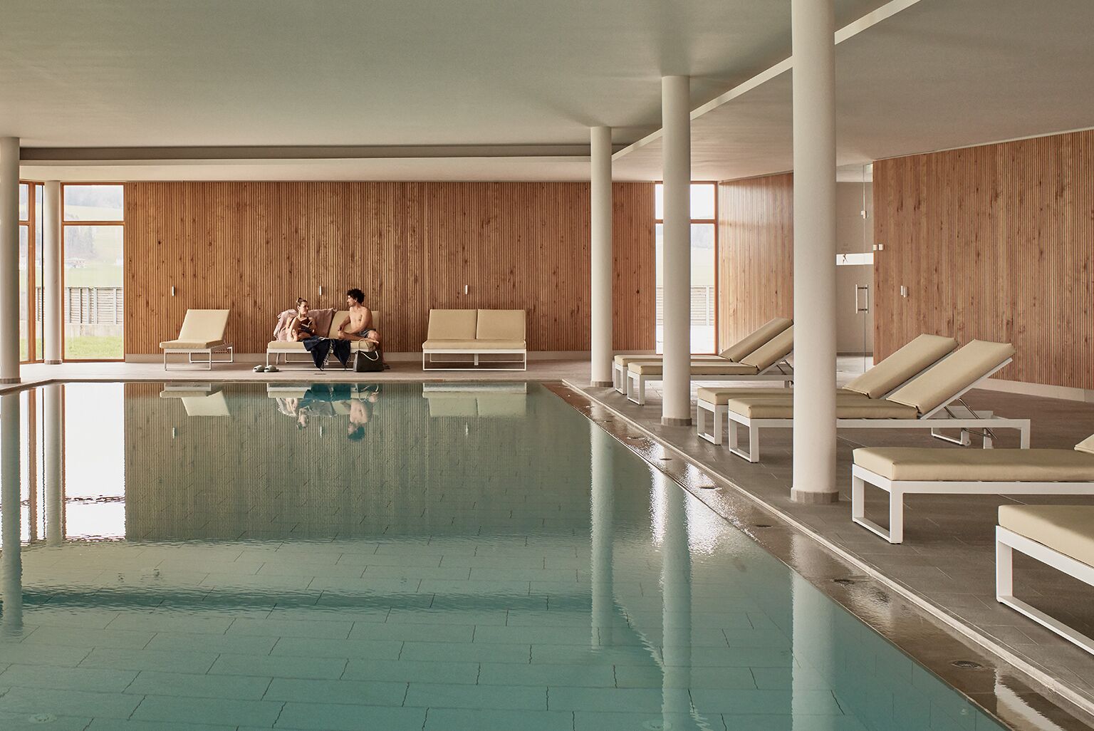An indoor swimming pool with lounge chairs and wooden panel walls.