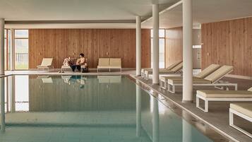 An indoor swimming pool with lounge chairs and wooden panel walls.