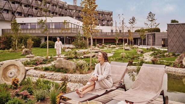 A spa area with two lounge chairs, a stone pathway, and a building with a unique architectural design in the background.