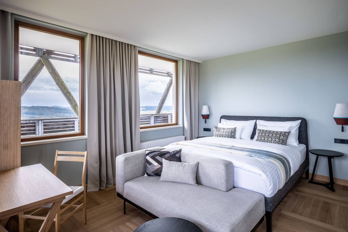 Een moderne hotelkamer met een bed, een bureau en uitzicht op een brug en het landschap.
