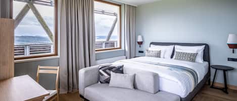 A modern hotel room with a bed, a desk, and a view of a bridge and landscape.