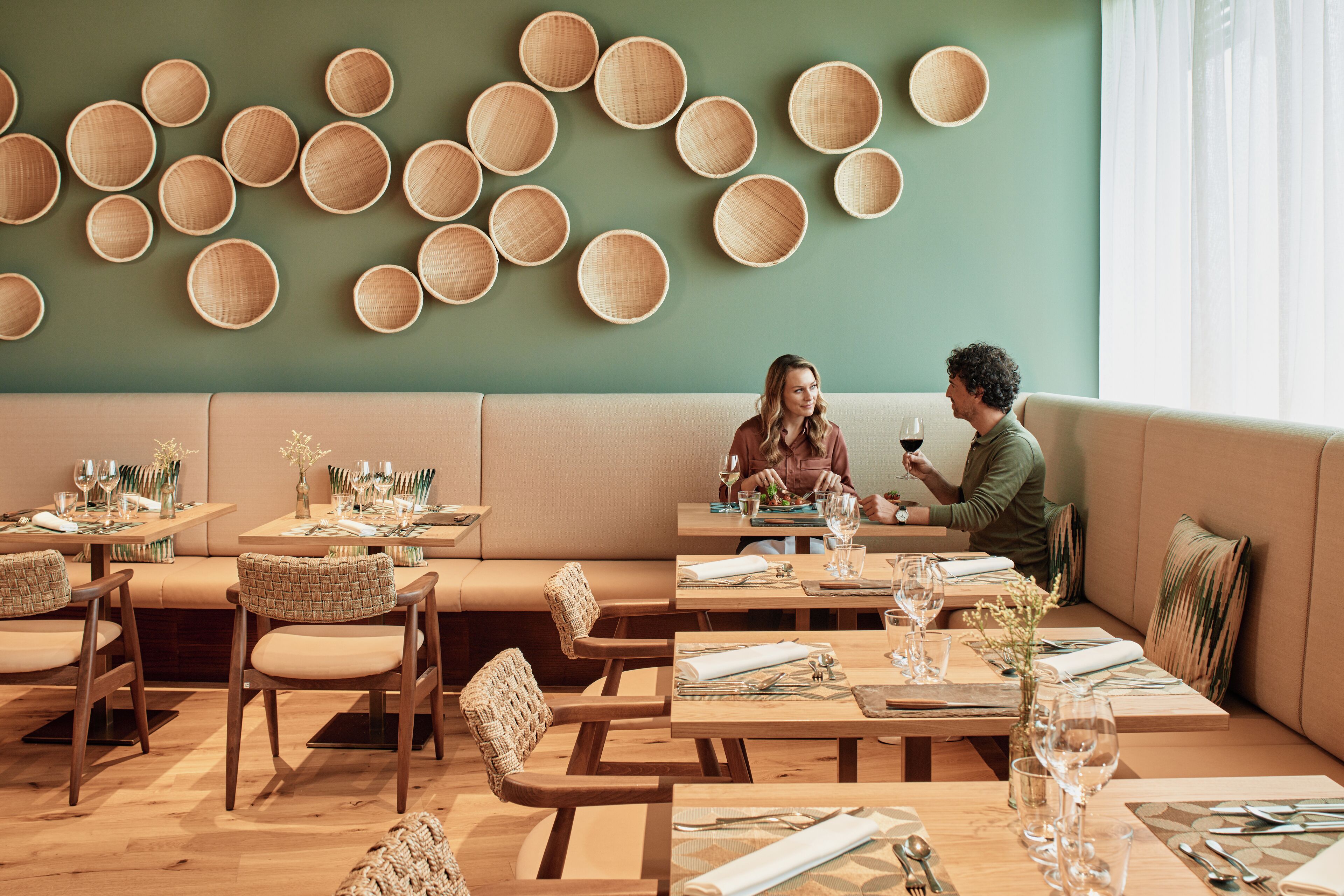 En restaurant med flere borde og siddepladser, kurvefletkurve på væggen og en grøn væg.