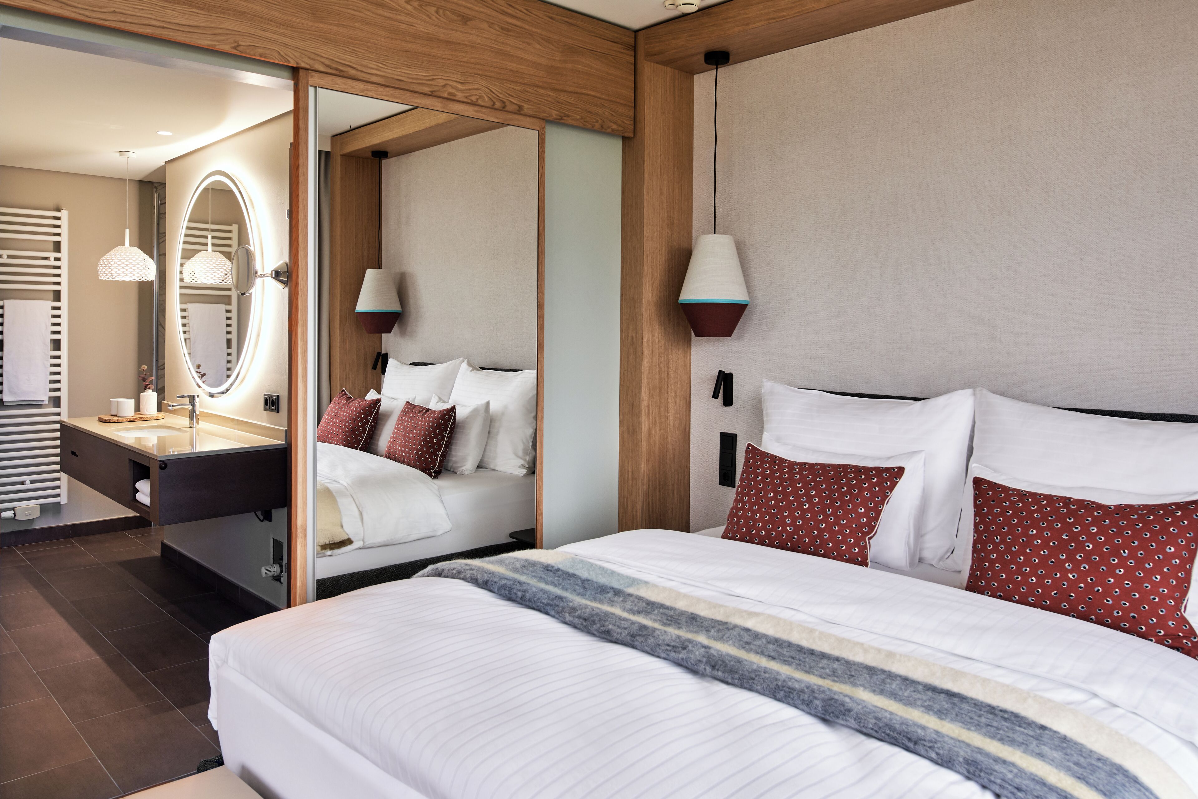 A hotel room with a large bed, a mirror, a vanity with a sink, and a nightstand.