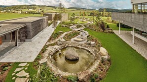 A modern building with a stone pathway leading to a circular water feature surrounded by a well-maintained garden.
