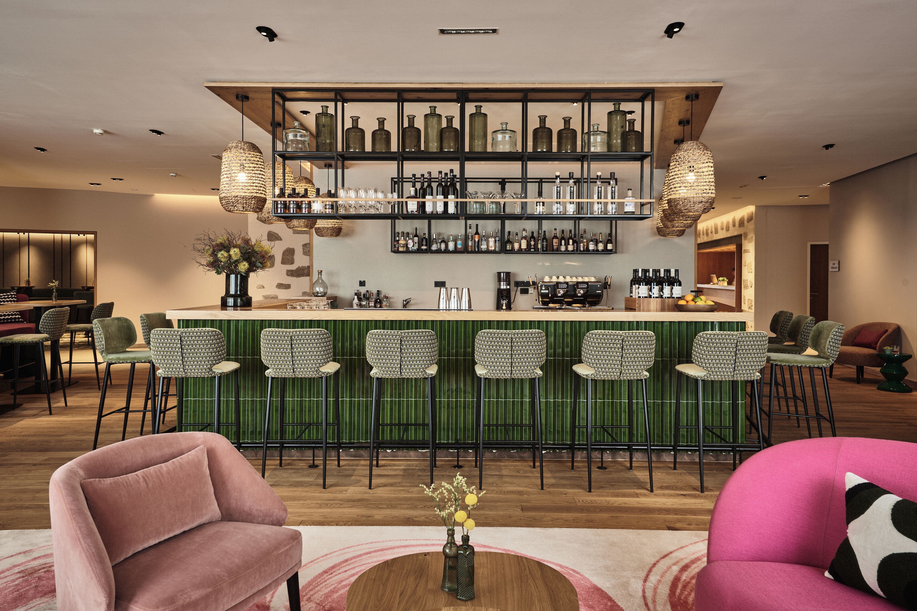 A bar area with a green bar counter, multiple stools, and shelves with bottles.