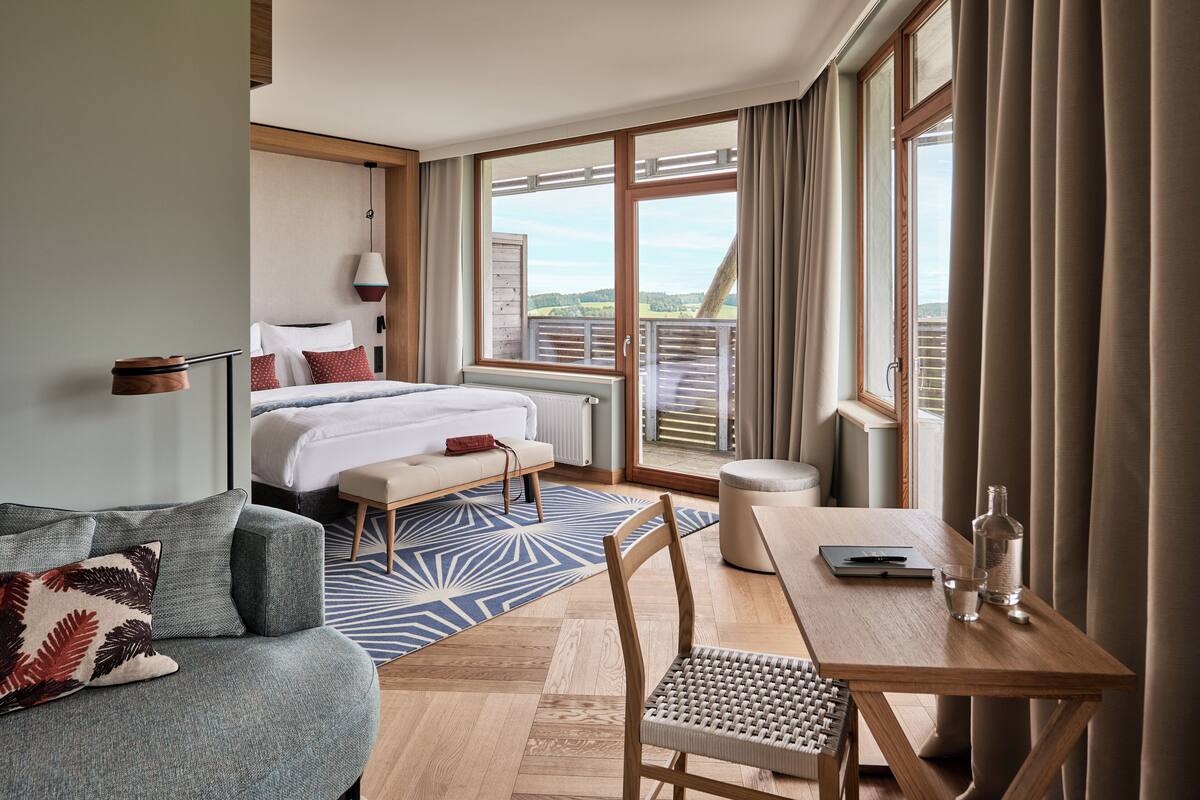 Een hotelkamer met een bed, een sofa, een eettafel en uitzicht op het groen.