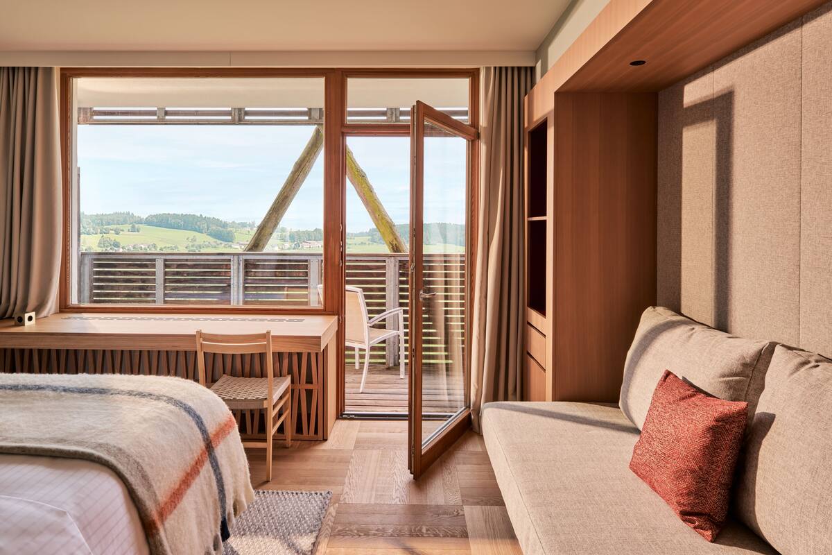 Een hotelkamer met een bed, een bank, een eettafel en uitzicht op een brug en het landschap.