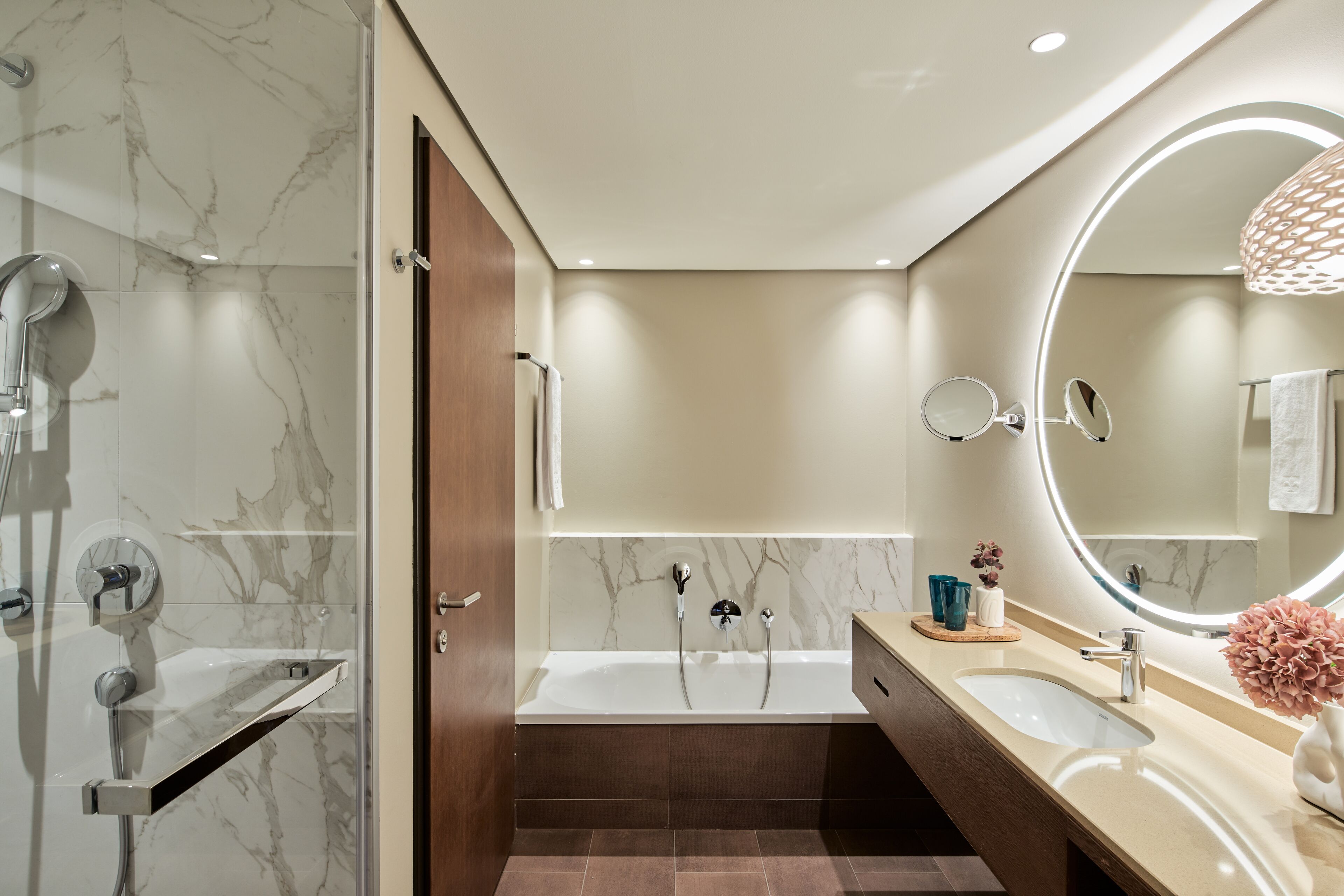 Un baño moderno con ducha de mármol, bañera, tocador con espejo y lavabo.
