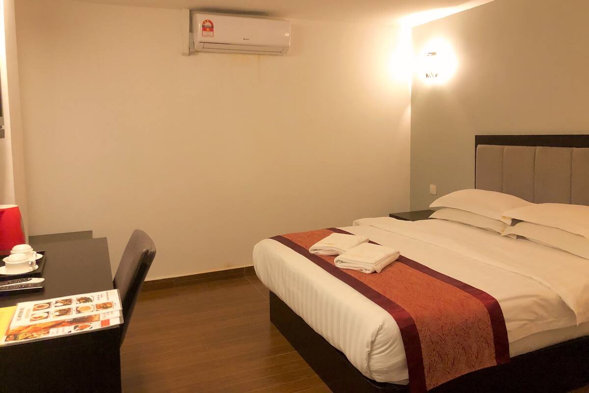 A hotel room with a bed, a desk with a chair, and an air conditioning unit on the wall.