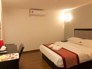 A hotel room with a bed, a desk with a chair, and an air conditioning unit on the wall.