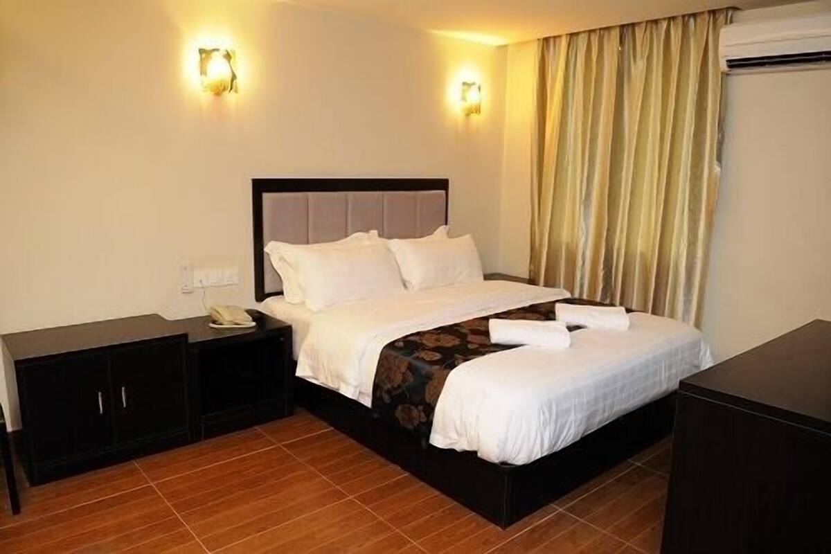 A hotel room with a bed, nightstand, and a wardrobe.