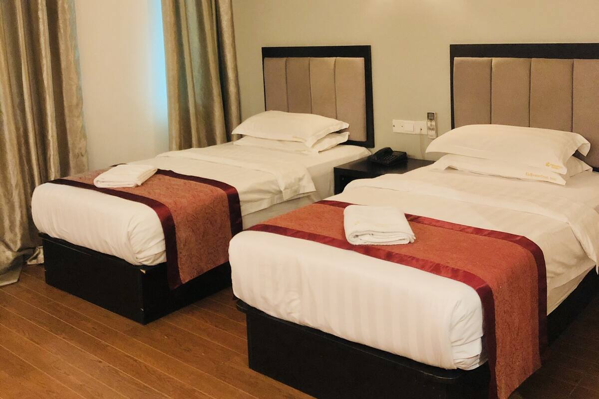 A hotel room with two beds, each with a headboard, a bedside table, and a lamp.