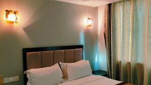 Une chambre d’hôtel avec un grand lit, deux lampes fixées au mur, une tête de lit et un rideau.