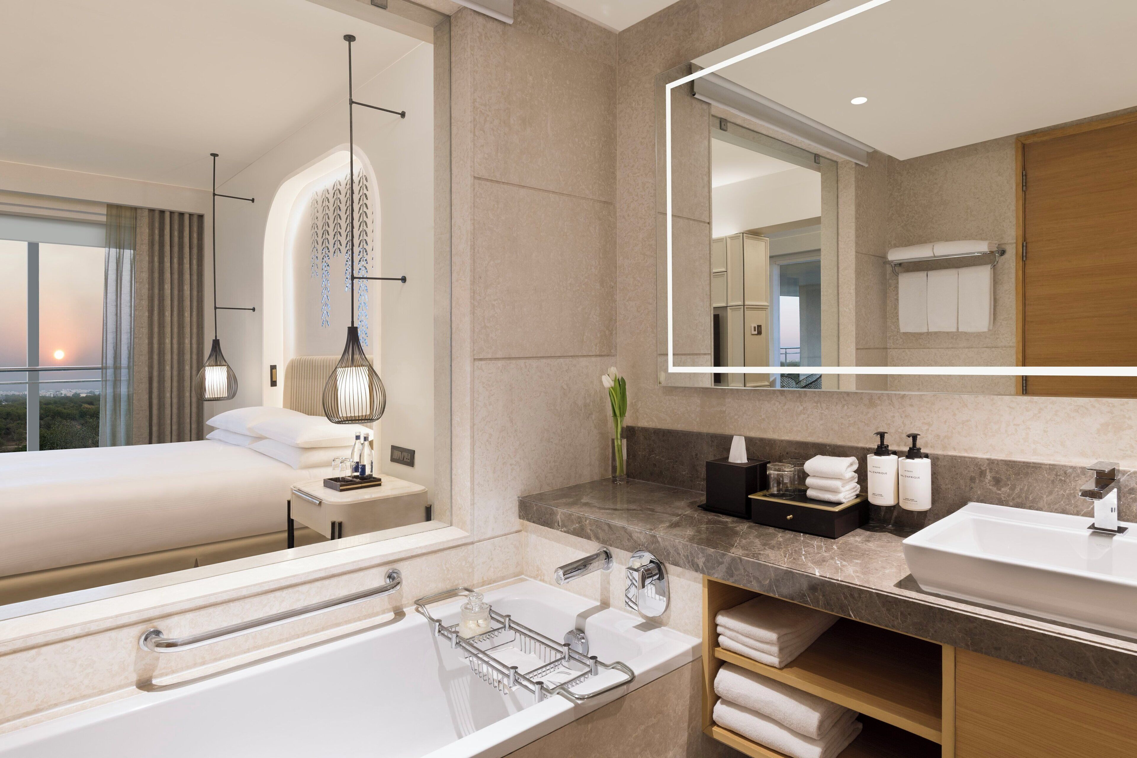 Une chambre d’hôtel moderne avec un grand lit, une salle de bain avec baignoire, une coiffeuse avec miroir et une vue sur la ville.