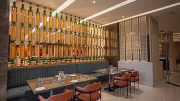 A modern restaurant with a long counter, cushioned seating, and decorative hanging lights.