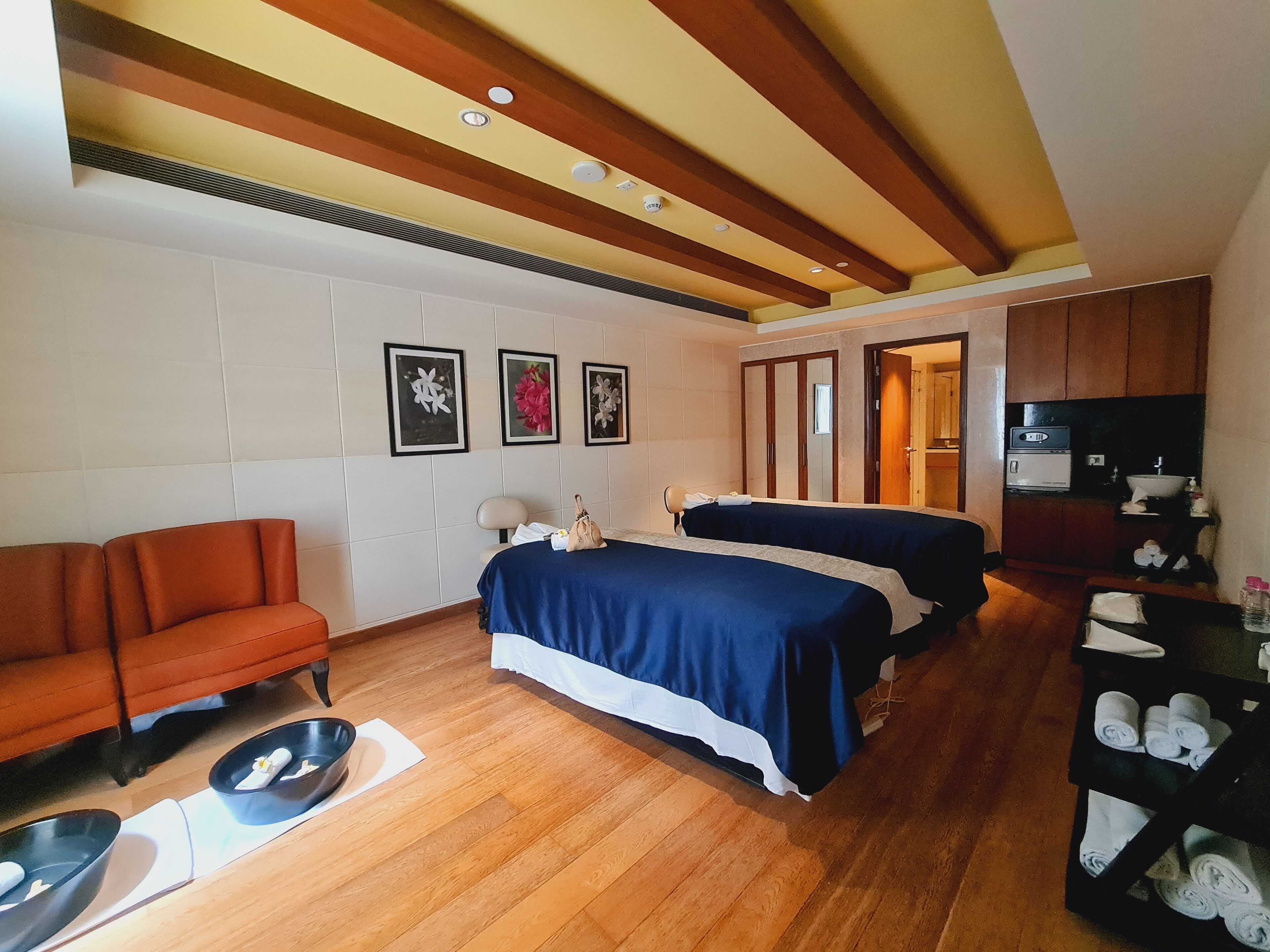 A hotel room with two beds, a sofa, a wooden floor, and a kitchenette.