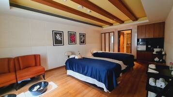 A hotel room with two beds, a sofa, a wooden floor, and a kitchenette.