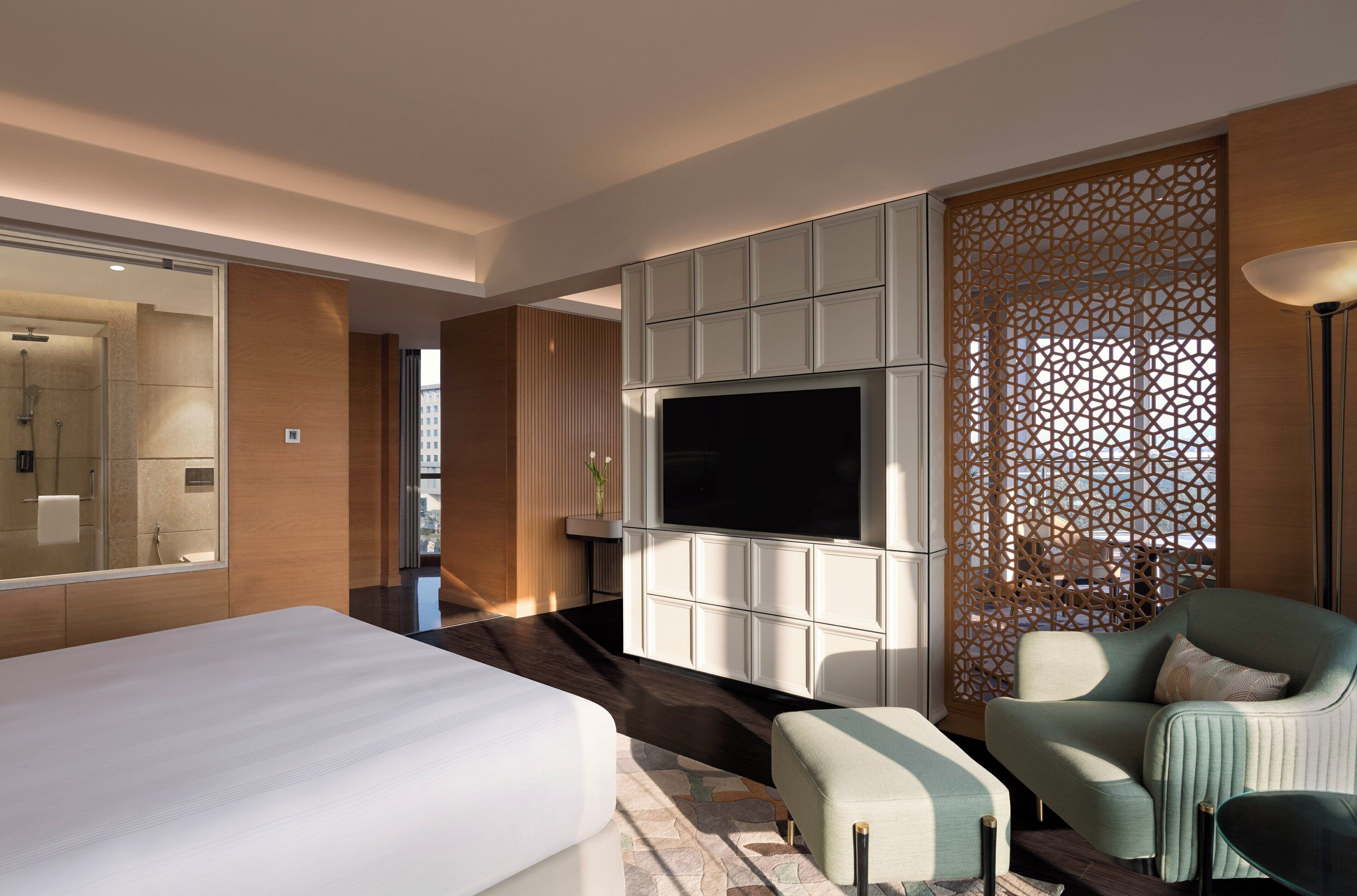 A hotel room with a large bed, a TV, a seating area, and a decorative partition.