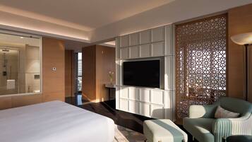 A hotel room with a large bed, a TV, a seating area, and a decorative partition.