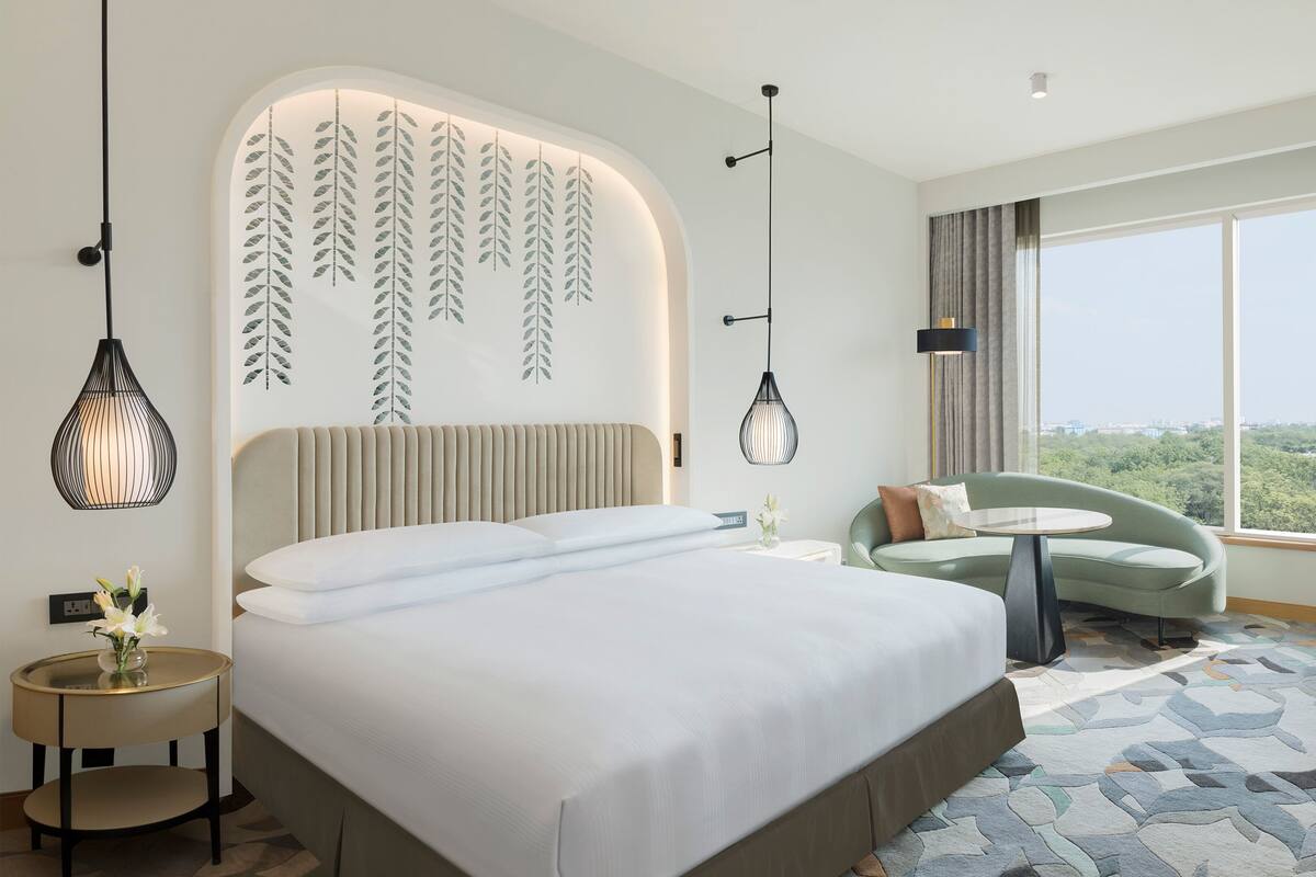 Een moderne hotelkamer met een groot bed, een zithoek met uitzicht en decoratieve bladwandkunst.