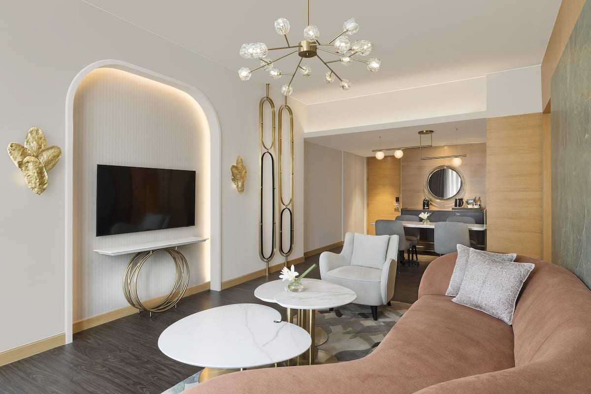 Een moderne woonkamer met een flatscreen televisie, een ronde salontafel, een bank en een eethoek op de achtergrond.