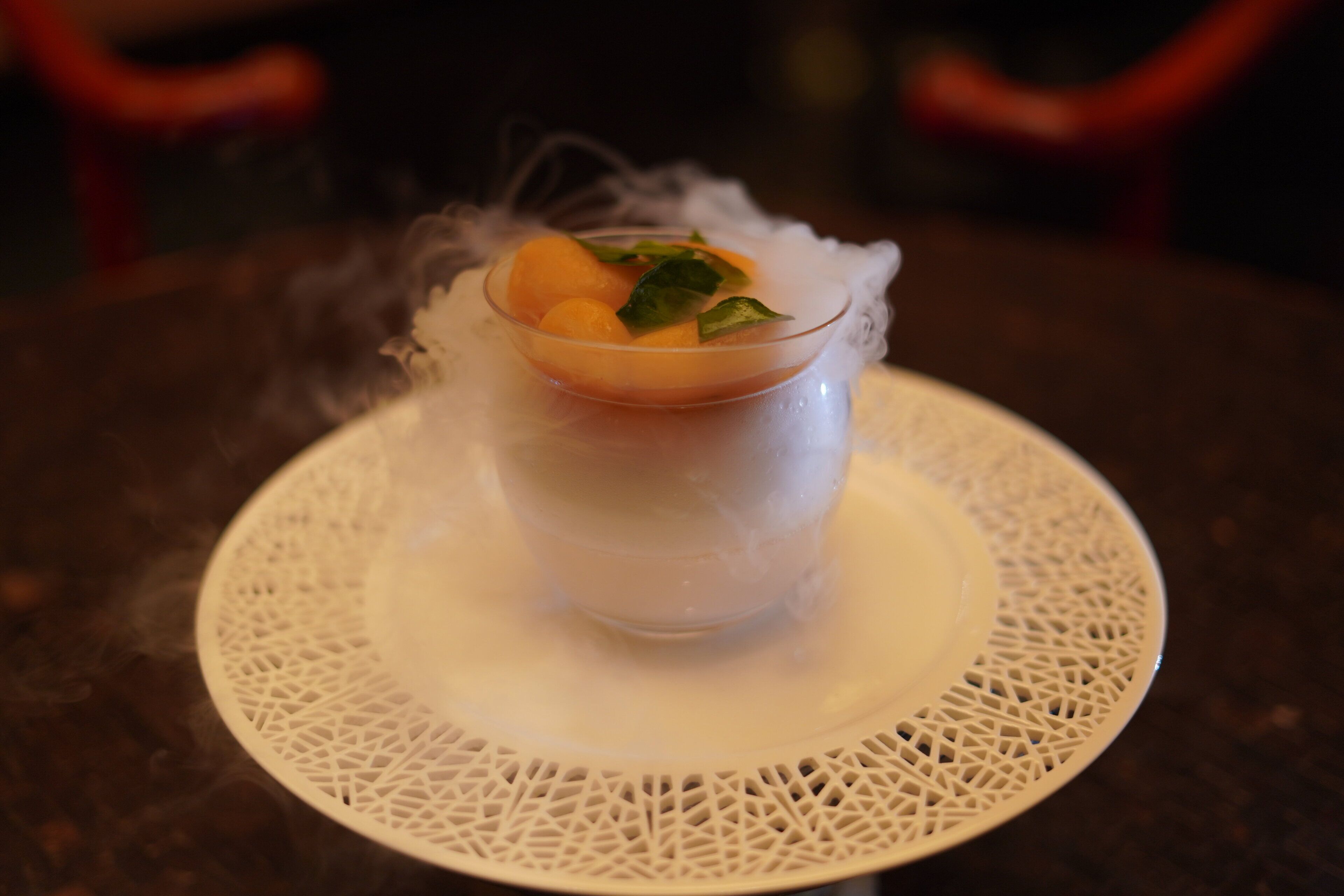 Et gennemsigtigt glas med dessert på en hvid tallerken med blondekant.
