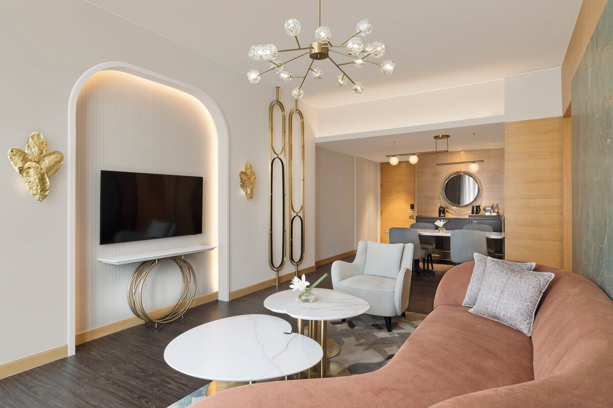Ein modernes Wohnzimmer mit Flachbildfernseher, rundem Couchtisch, Sofa und Essbereich im Hintergrund.