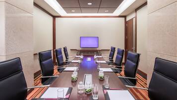 A conference room with a long table, black chairs, and a television screen at the front.