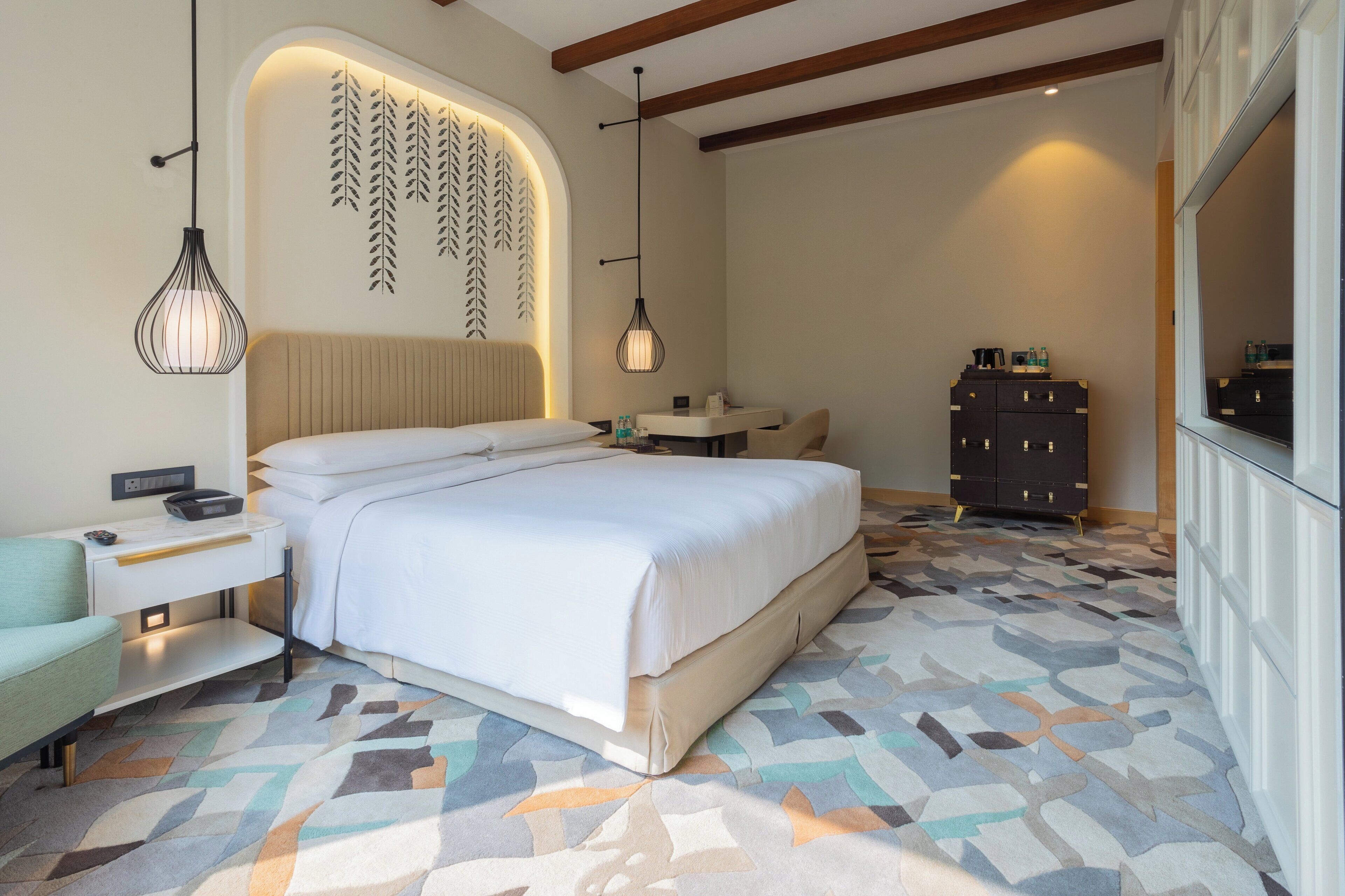 A modern bedroom with a large bed, bedside tables, a dresser, and a patterned carpet.