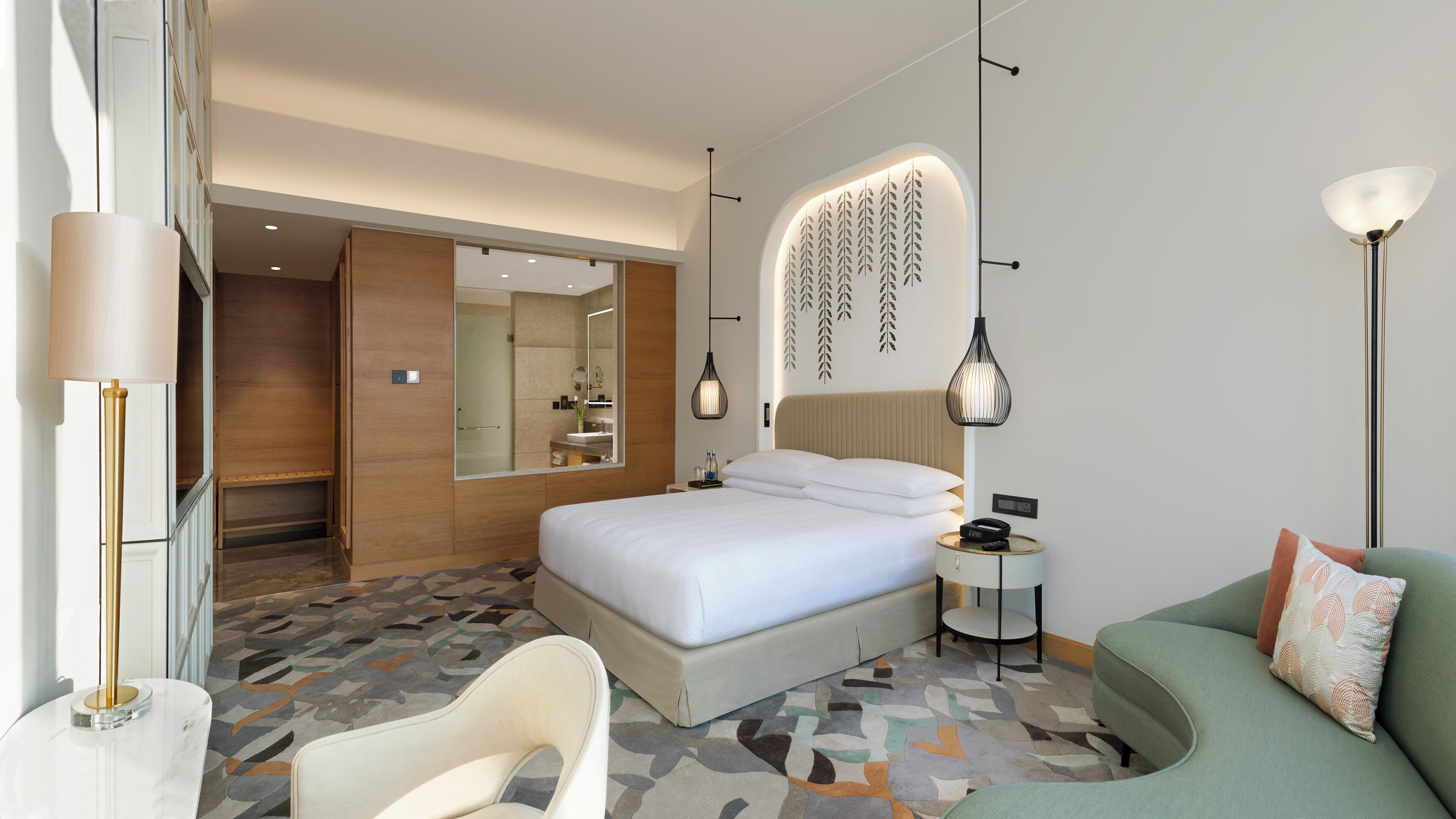 A modern hotel room with a large bed, a sofa, a small table, and a mirror.