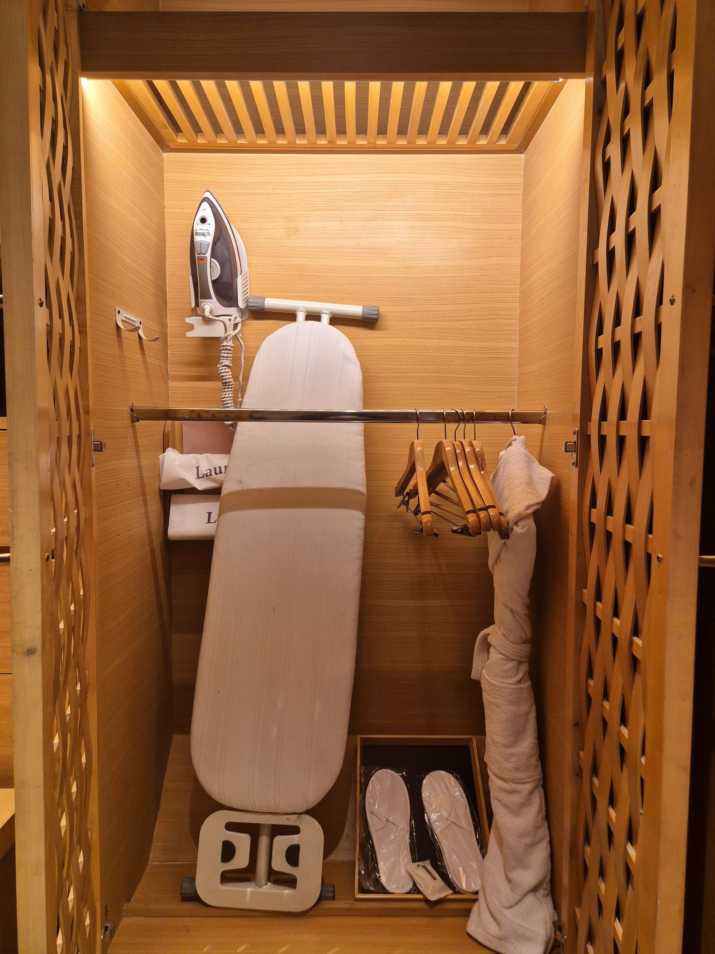 Habitación funcional con detalles de madera, que incluye una plancha de pared, un perchero para zapatos y un par de zapatillas en el suelo.