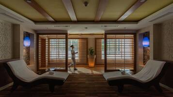 Relax in a serene spa room with a lounge area, featuring two comfortable chairs, a potted plant, and large windows.