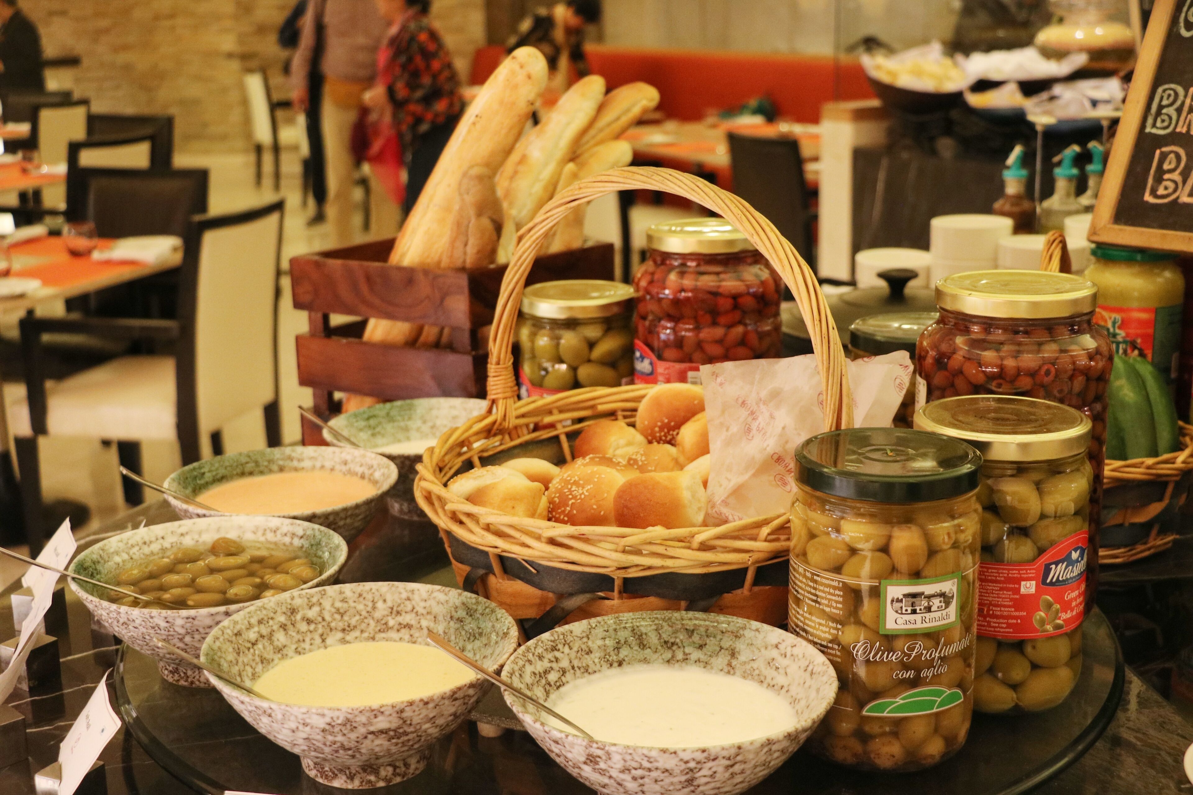 A buffet table with various food items including bread, olives, and jars of preserves.