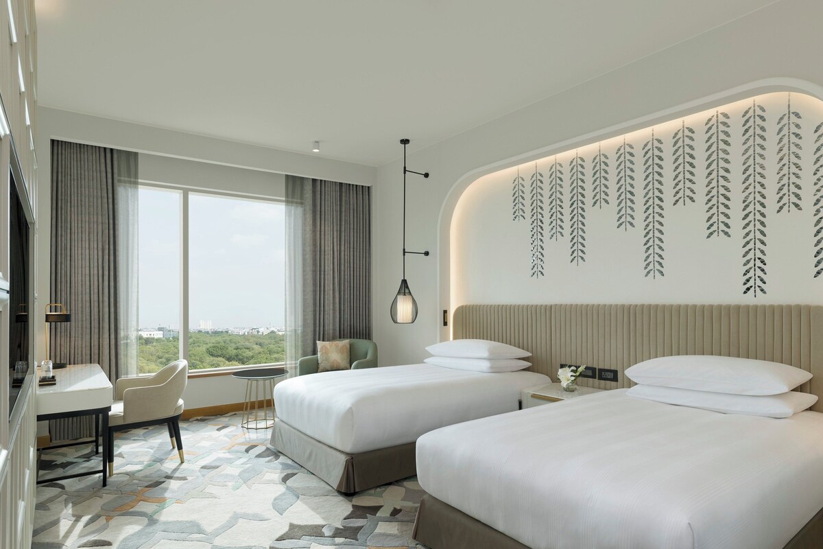 Ein modernes Hotelzimmer mit zwei Betten, einem Schreibtisch und einem großen Fenster mit Blick auf die Stadt.