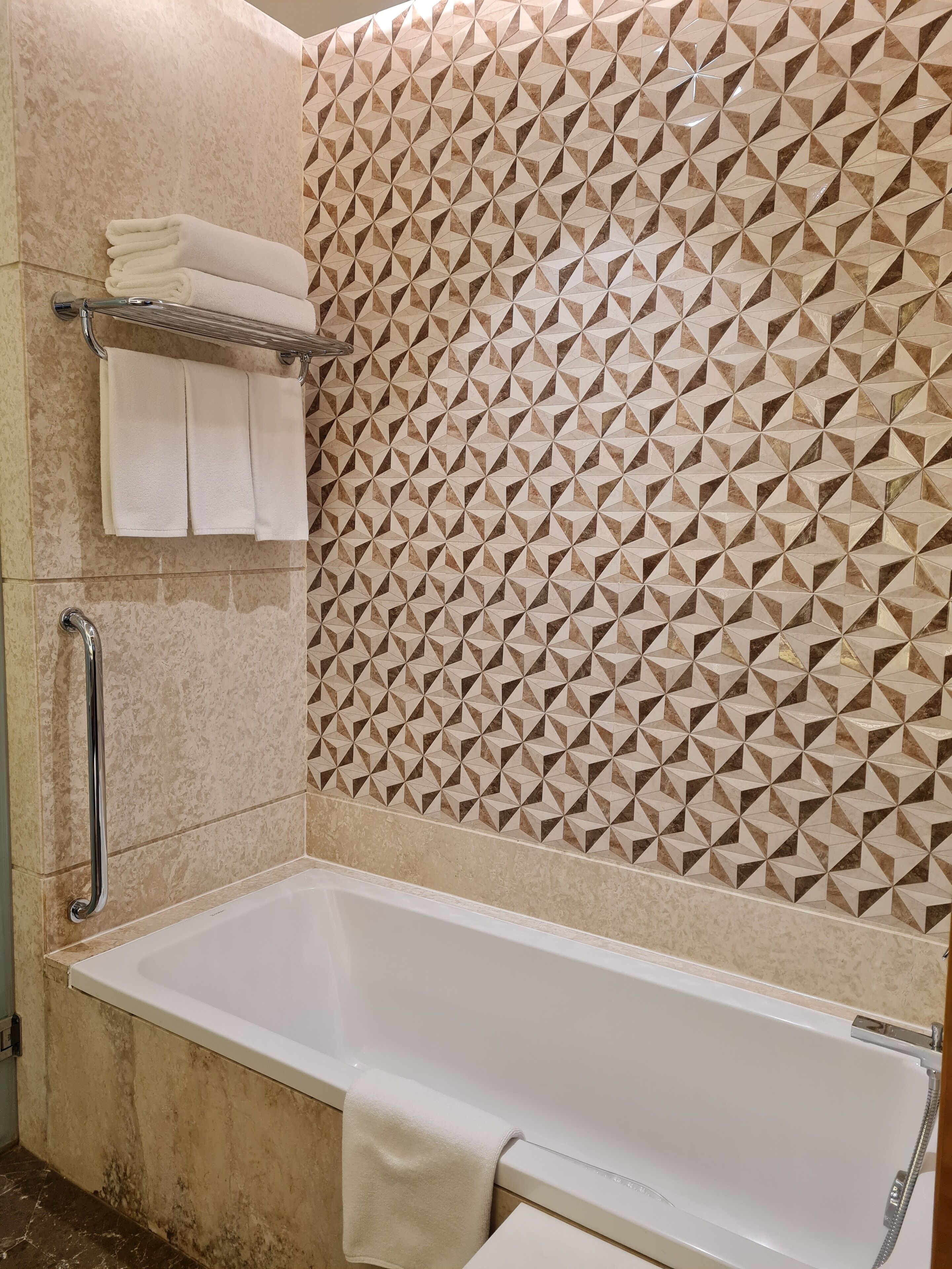 A bathroom with a white bathtub, a shower, and a handrail. There is a towel rack with folded towels.