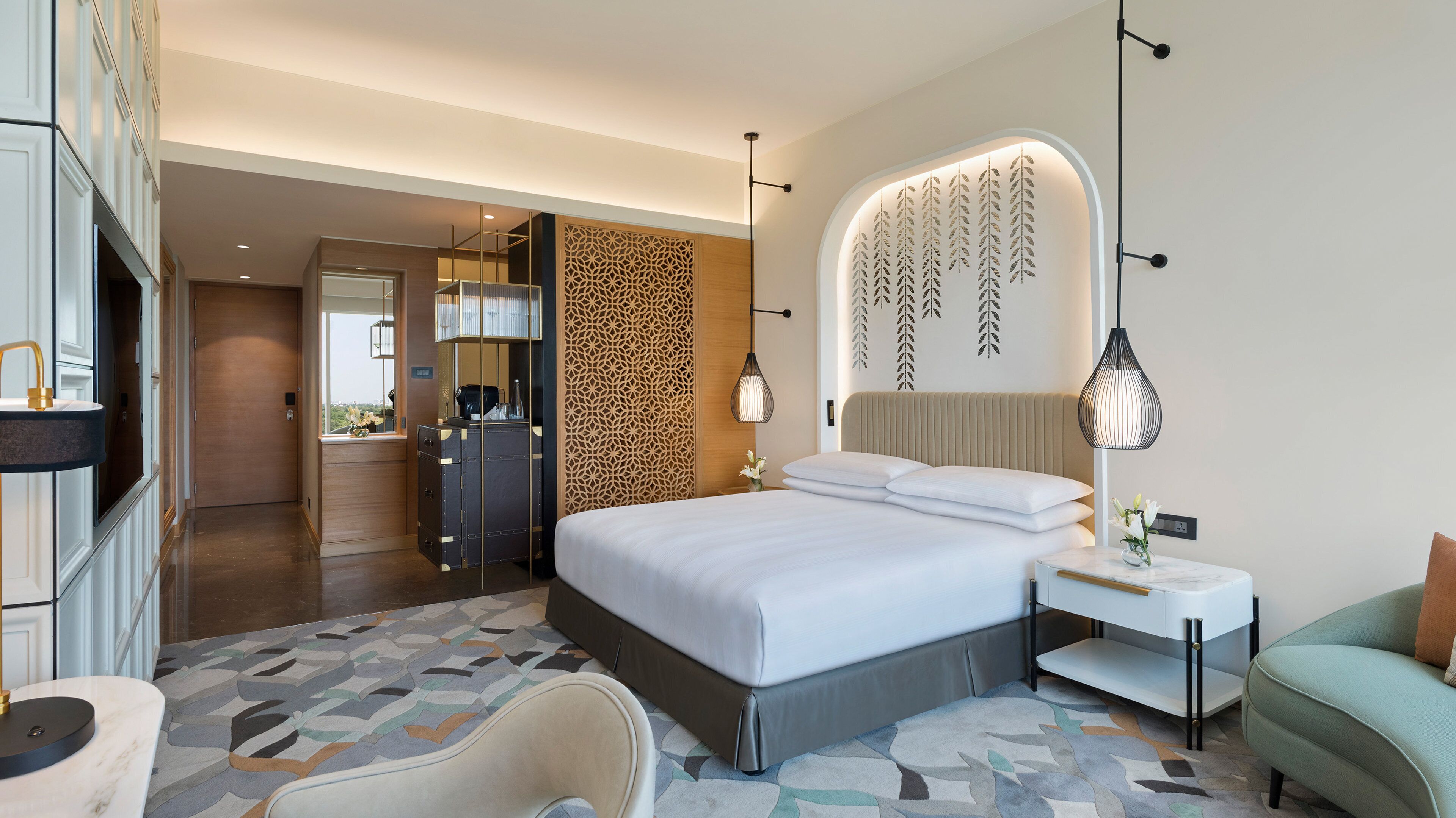Une chambre d’hôtel avec un grand lit, une table de chevet avec une lampe, une chaise et une vue sur le couloir.